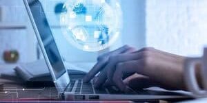 Side view and close up of businessman using laptop with digital globe projection, placed on office desktop with various items. Communication concept